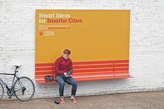 there is a man sitting on a bench in front of a wall with an advertisement