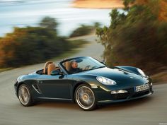 a black sports car driving down a road next to the ocean