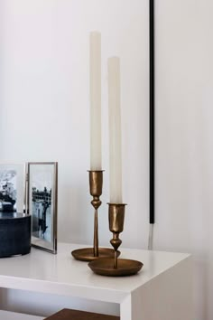 two candles are sitting on a white table next to a black and white framed photograph