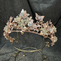 a tiara with butterflies on it sitting on top of a metal stand in front of a black background