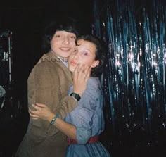 two young women hugging each other in front of tinsel foil curtained backdrops