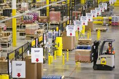 a warehouse filled with lots of boxes and forklifts driving down it's side