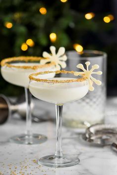 two glasses filled with white liquid on top of a table next to a christmas tree