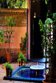 an outdoor courtyard with potted plants and water fountain in the center, surrounded by brick walls