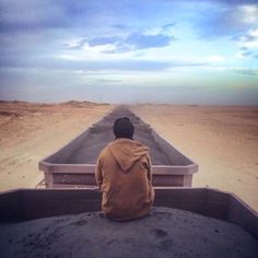 a person sitting in the back of a truck on top of a dirt road with a sky background