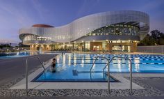 an empty swimming pool with people in it at night time, near a modern building