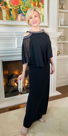 a woman standing in front of a fire place wearing a black dress with sheer shoulders