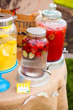 three jars filled with different types of drinks on top of a wooden table next to lemons and raspberries