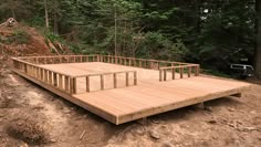 a wooden deck in the middle of a forest with lots of trees and dirt around it