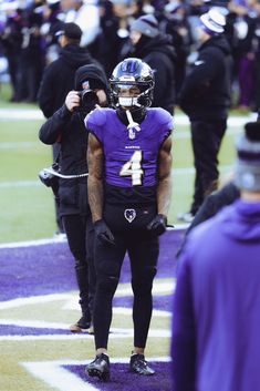 a football player walking on the field with other players in the background and people standing behind him