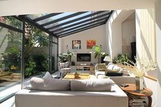 a living room filled with lots of furniture next to a large glass wall covered in plants