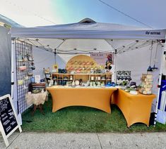 an outdoor market tent set up with various items for sale on the grass under it