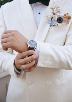 a close up of a person wearing a white suit and blue flowered boutonniere