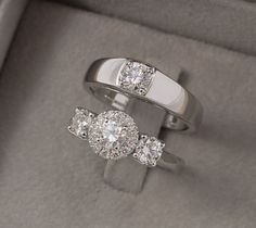 two diamond rings sitting in a box on top of each other, one with a center stone and the other with three smaller round diamonds