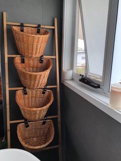 four wicker baskets are stacked on a ladder in front of a bathroom window, next to a toilet