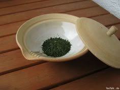 a white bowl filled with green stuff on top of a wooden table