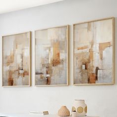 two abstract paintings hang on the wall above a white table with vases and books