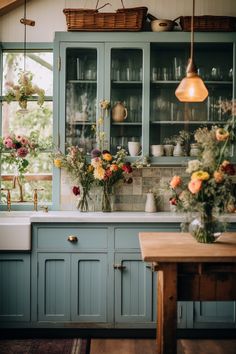 a kitchen with blue cabinets and flowers in vases on the counter top, next to a wooden table