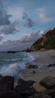 waves crashing on the beach and rocks under a cloudy sky at dusk, with an island in the background