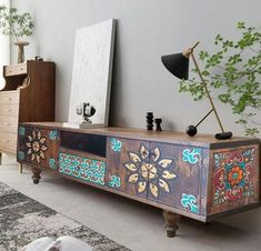 an artisticly painted sideboard in a living room with a plant on the floor