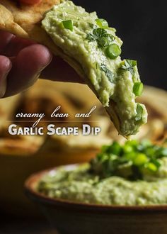 a person dipping guacamole into a bowl with chips and salsa in the background