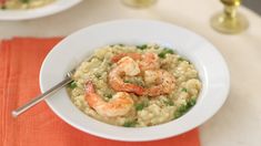 shrimp and rice with peas in a white bowl on an orange place mat next to two gold candles