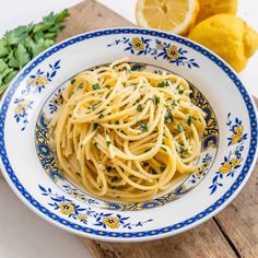 a white and blue bowl filled with pasta on top of a wooden table next to lemons