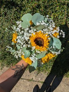 a bouquet of sunflowers and baby's breath is held by a man