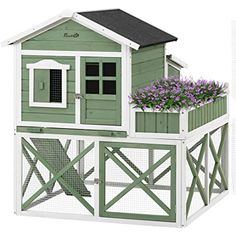 a green and white chicken coop with purple flowers in the window boxes on the roof