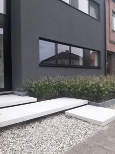 some white concrete steps in front of a gray building with windows and plants on the side