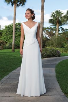 a woman in a white wedding dress standing on a sidewalk with palm trees behind her