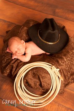 a baby laying on top of a brown blanket next to a cowboy hat and rope