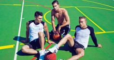 three men sitting on a basketball court with one holding a ball and the other kneeling down