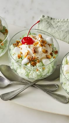 two bowls filled with food on top of a white plate next to silver spoons