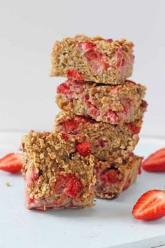 strawberry oatmeal bars stacked on top of each other with strawberries scattered around