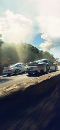 two silver sports cars driving down a road next to each other on a sunny day