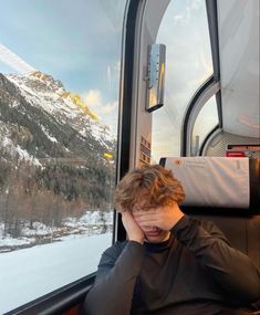 a man sitting on a train with his head in his hands while looking out the window