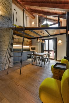 an open living room and dining area with wood flooring, exposed ceiling beams, yellow chairs and a loft bed