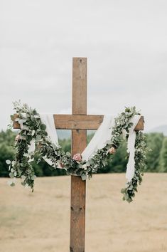 a cross decorated with flowers and greenery for a wedding ceremony in the country side