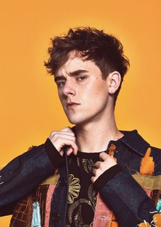 a young man is holding onto his jacket and looking at the camera while standing in front of an orange background