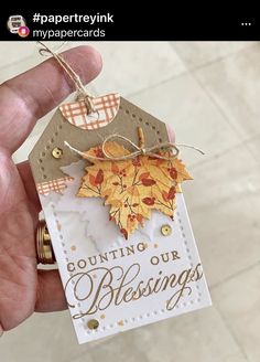 a hand holding a small tag with an autumn leaf on it that says counting our blessing