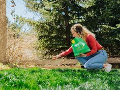 a woman kneeling down in the grass with a green bag