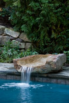 a large rock sitting next to a pool with water running down it's side