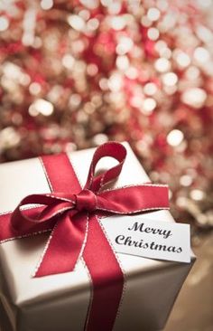 a white gift box with a red ribbon and merry christmas tag tied around the top