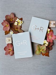 two wedding rings sitting next to flowers on a gray surface with the initials g + r