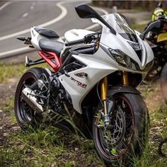 two motorcycles parked next to each other on the side of a road near grass and trees