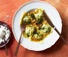 a white plate topped with ravioli next to a bowl of parmesan cheese