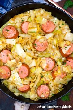 sausages and cabbage in a skillet on a wooden table next to some vegetables