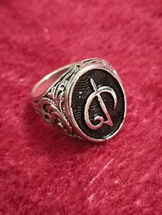 a silver ring with the letter d on it sitting on a red velvet surface in front of a pink background