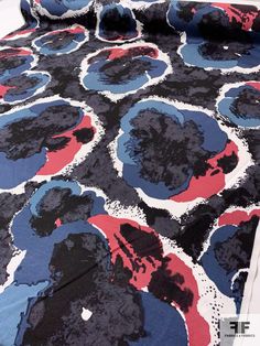 a bed covered in a blue, red and black bedspread with an abstract design